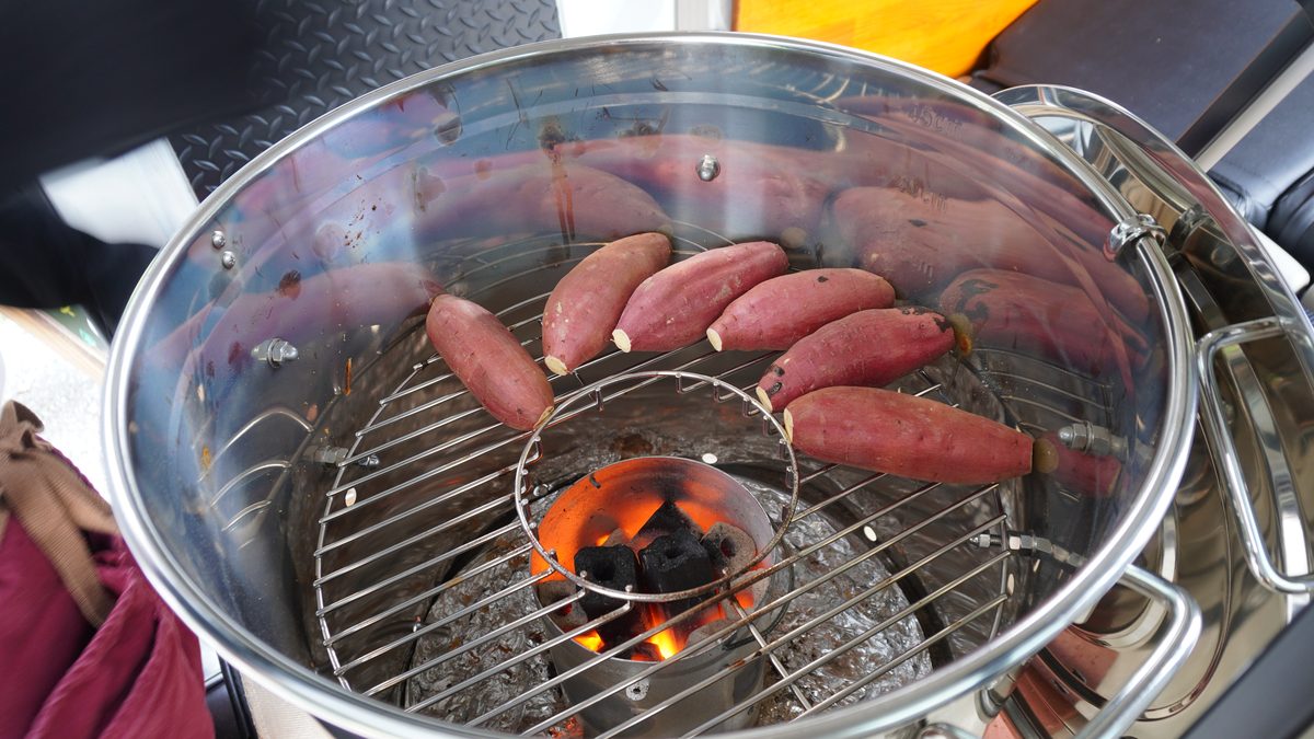 蓋を開けた焼き芋機の中。二段の焼き網に芋を並べ、中央の炭かごで炭火が燃えている