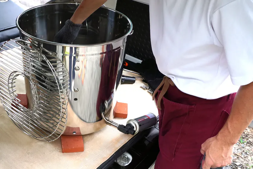 軽バンの荷台で、えんじ色のエプロン姿で炭かごとステンレスの窯を手で組み上げる代表