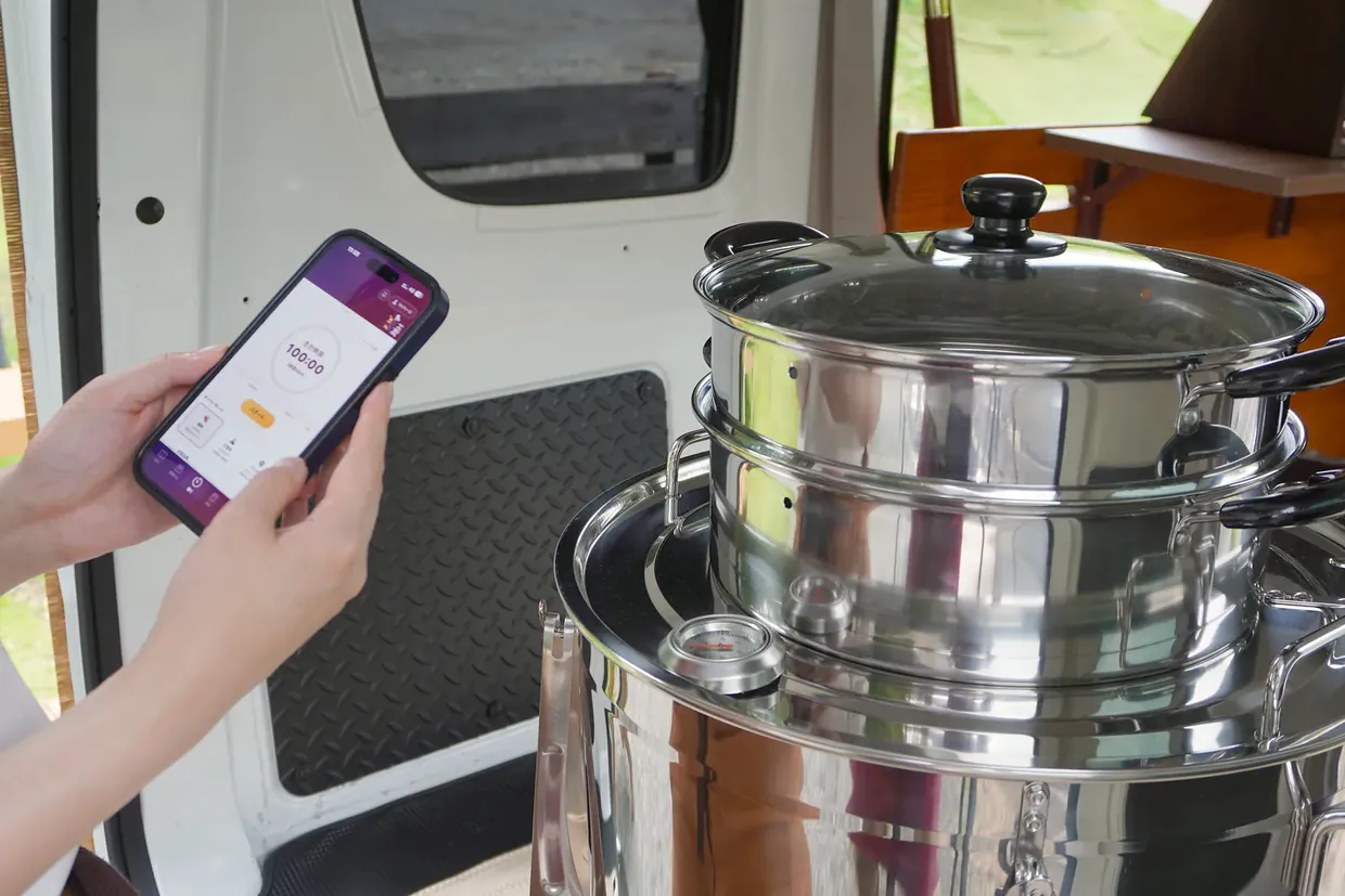 肩越しに見た、焼き芋機の前でオーナーアプリを開くスマートフォン
